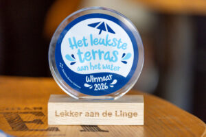 Seijbel Photography- -0529 - Stichting Bureau Toerisme - Stichting Bureau Toerisme Round glass award with a blue ring, displaying 'Het leukste terras aan het water' and 'Winnaar 2026' on a wooden stand.